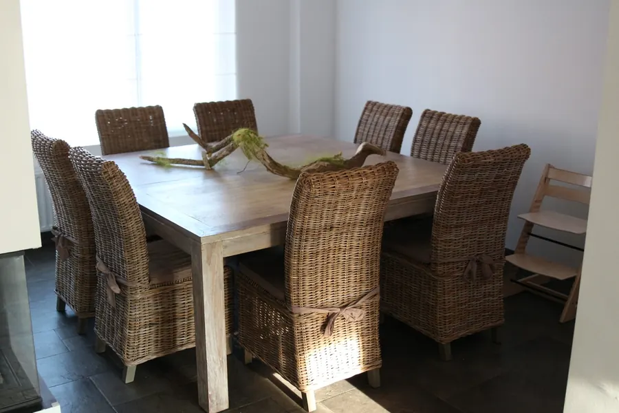 Een vierkante eiken eettafel met acht rieten stoelen en een kinderstoel