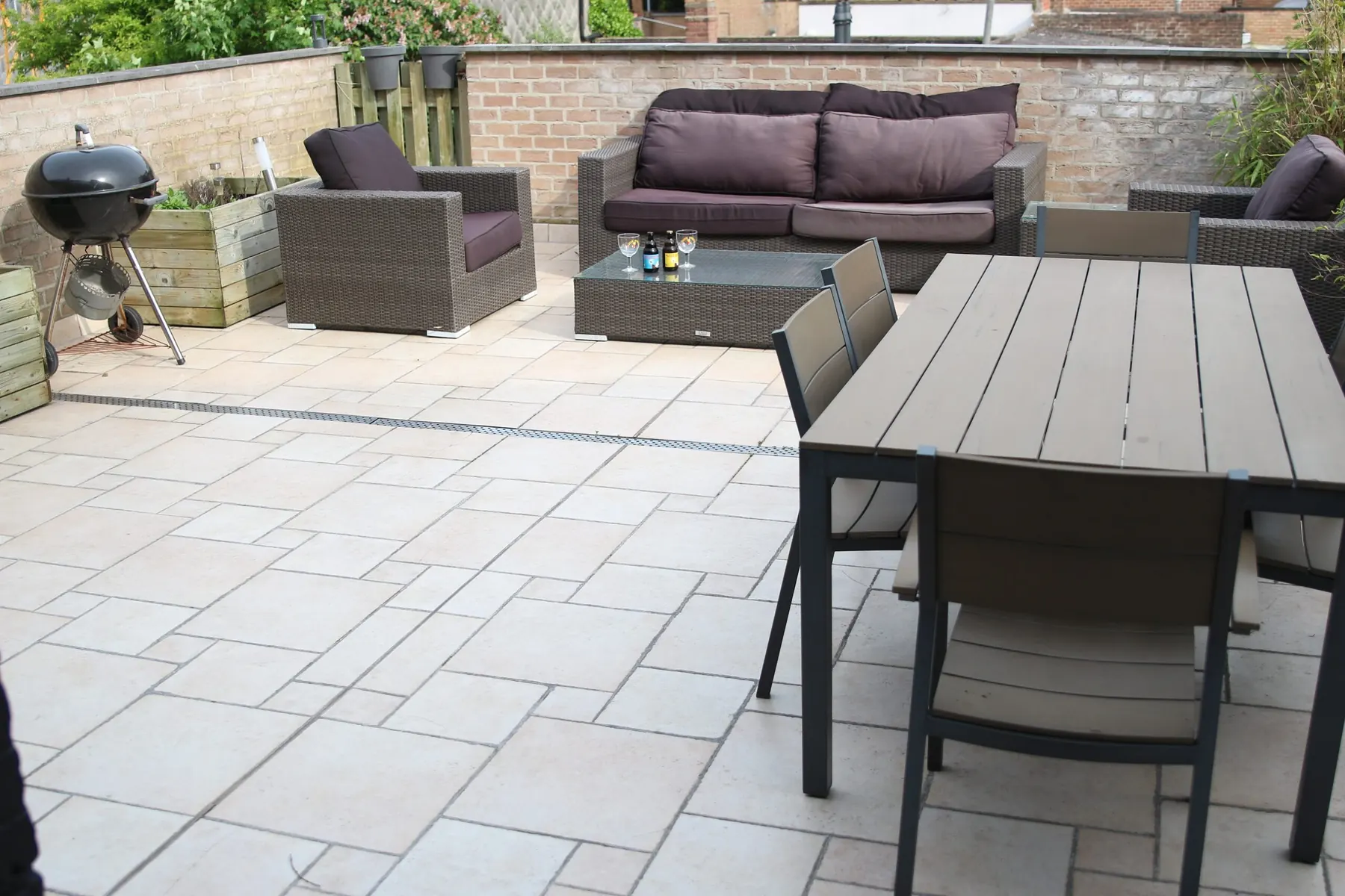 Die ummauerte Terrasse mit Loungemöbeln, Esstisch und Holzkohlegrill